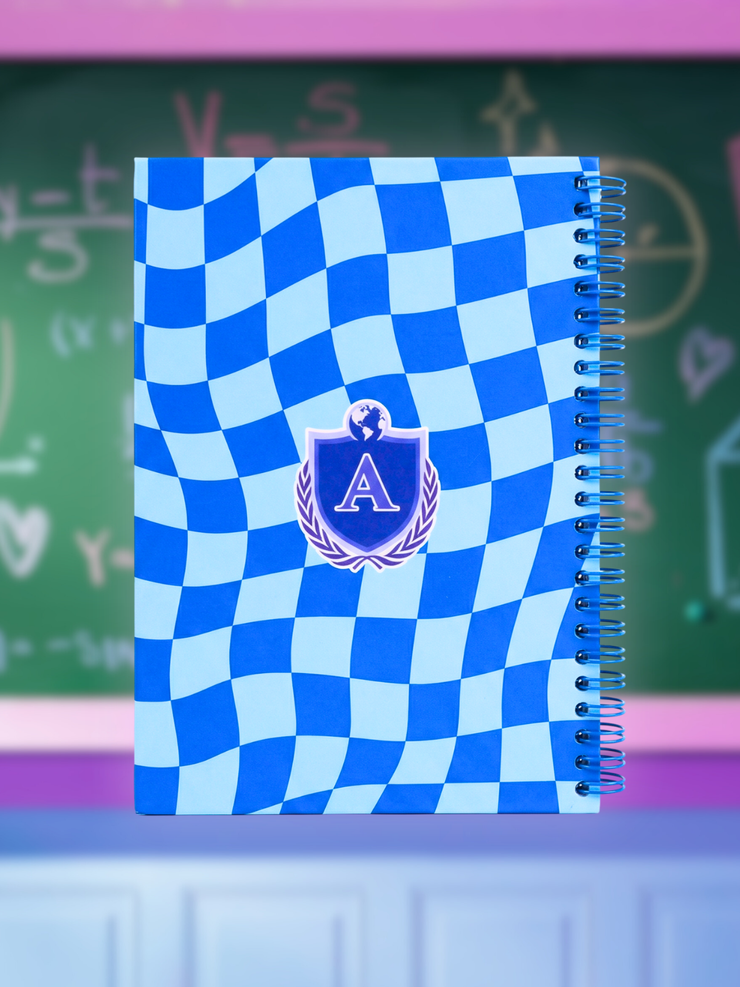 Notebook with blue checkered design and emblem on a green chalkboard background - Alans Universe